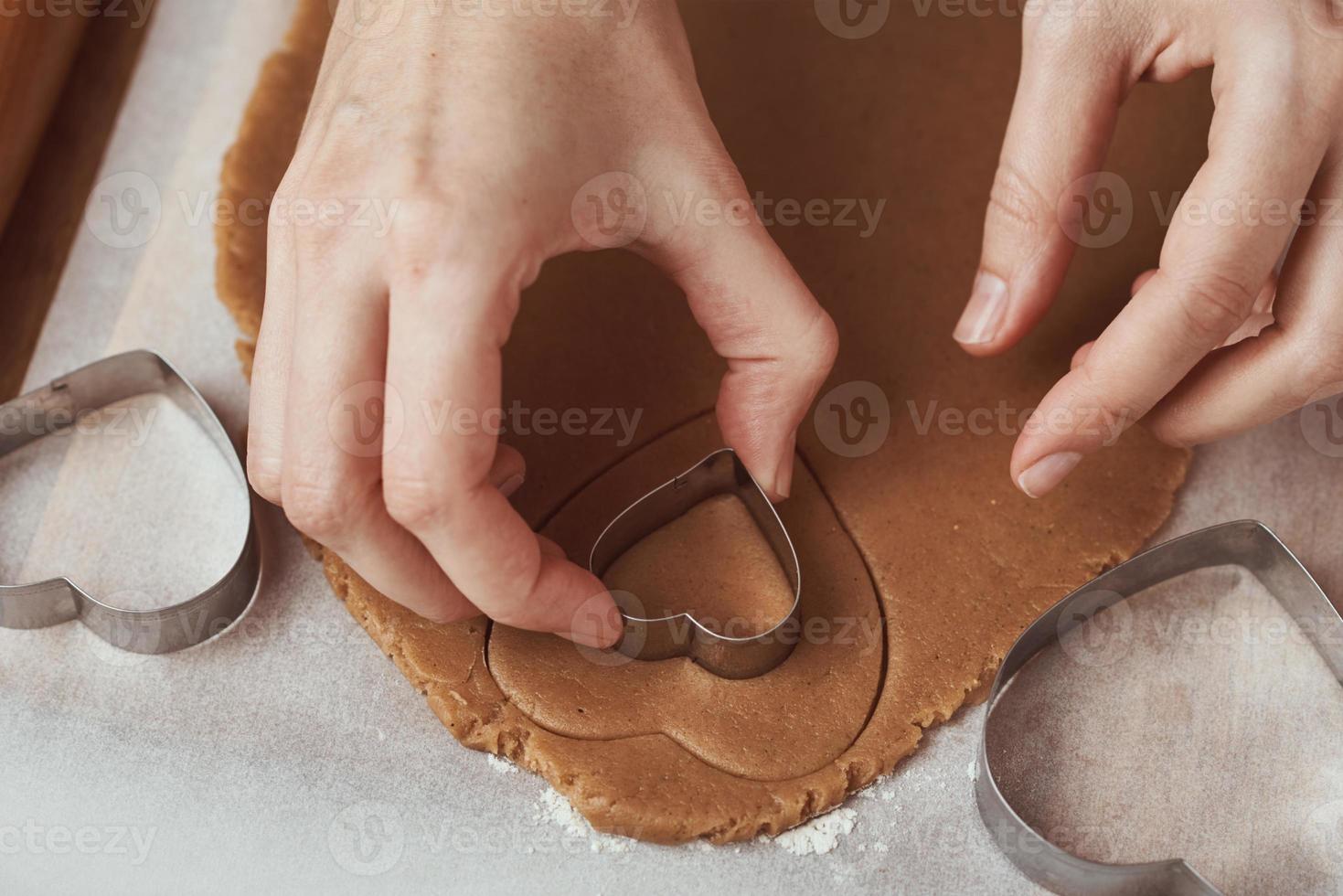 fabbricazione Pan di zenzero biscotti nel il forma di un' cuore per san valentino giorno. donna mano uso biscotto taglierina. vacanza cibo concetto foto