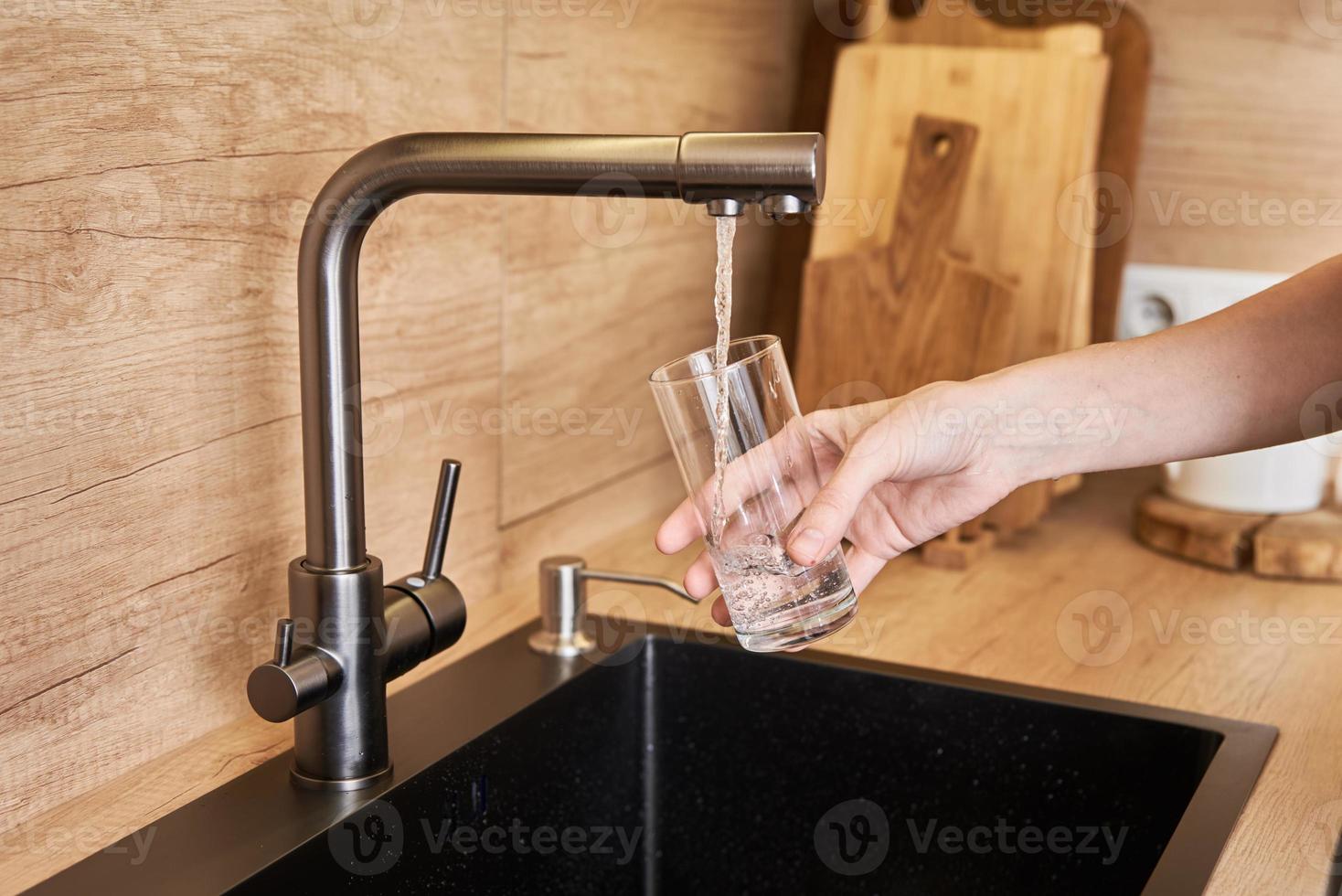 donna versare pulito acqua a partire dal rubinetto filtro in un' bicchiere foto