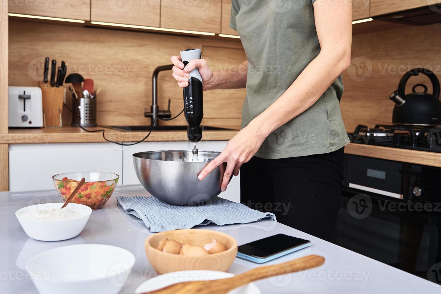 donna nel cucina cucinando un' torta. mani battere il Impasto con un elettrico miscelatore foto