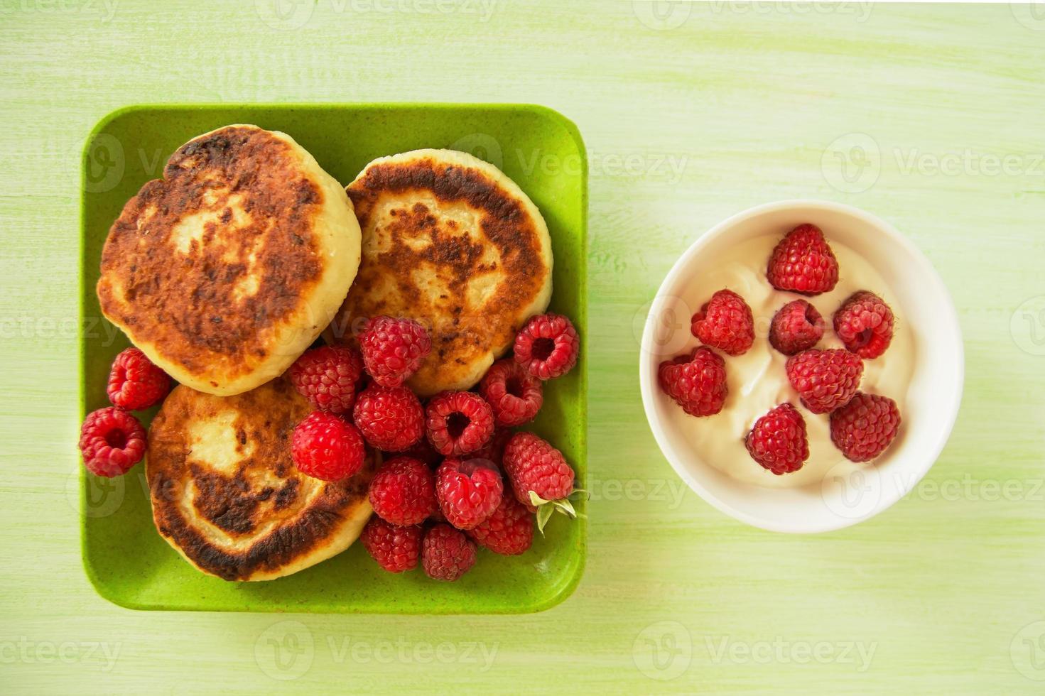 Villetta formaggio Pancakes con fresco lamponi e acida crema su il verde e bianca piatti su il verde di legno sfondo, superiore Visualizza. foto