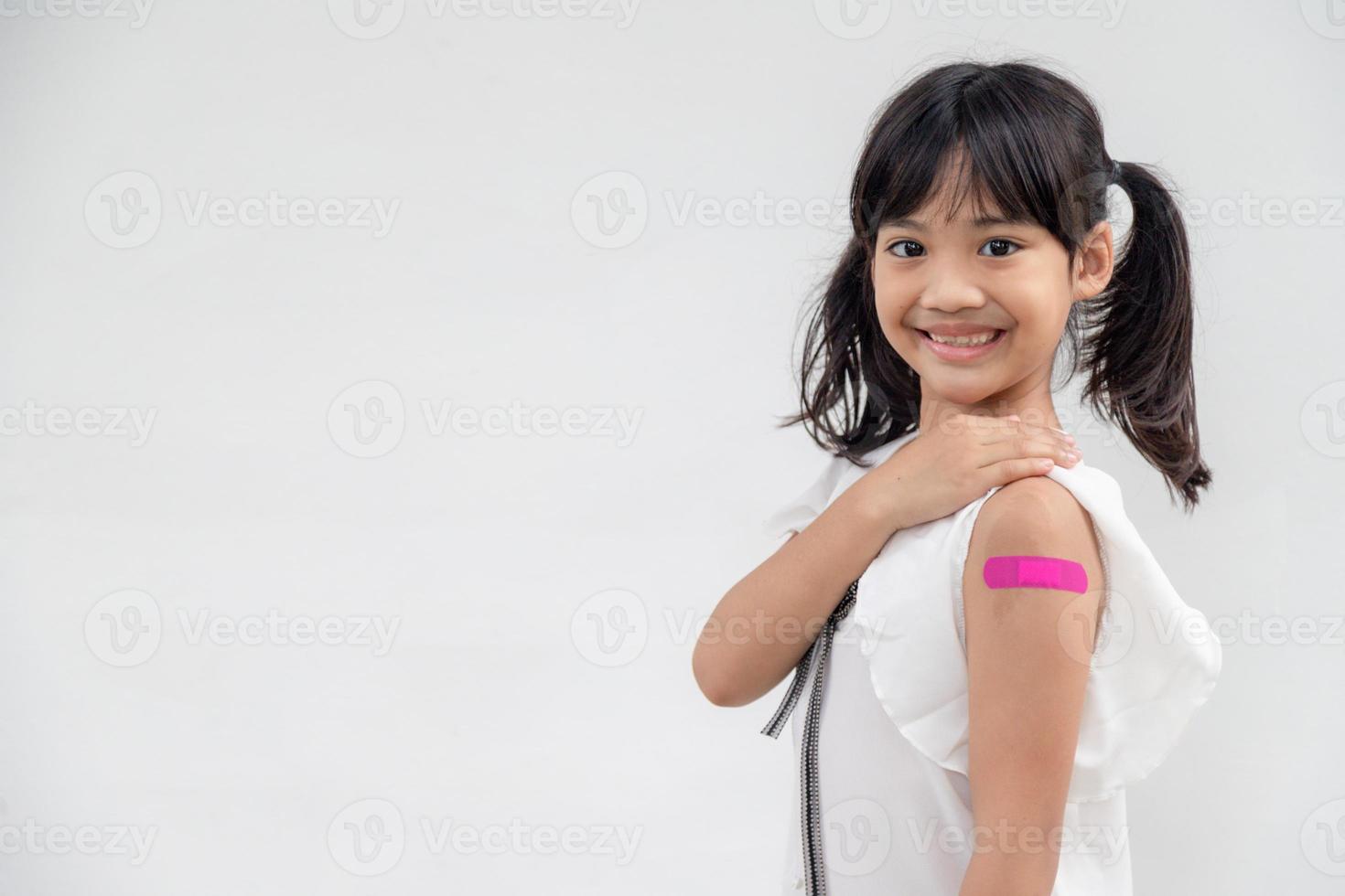 asiatico poco ragazza mostrando il suo braccio dopo avuto vaccinati o inoculazione, bambino immunizzazione, covid delta vaccino concetto foto