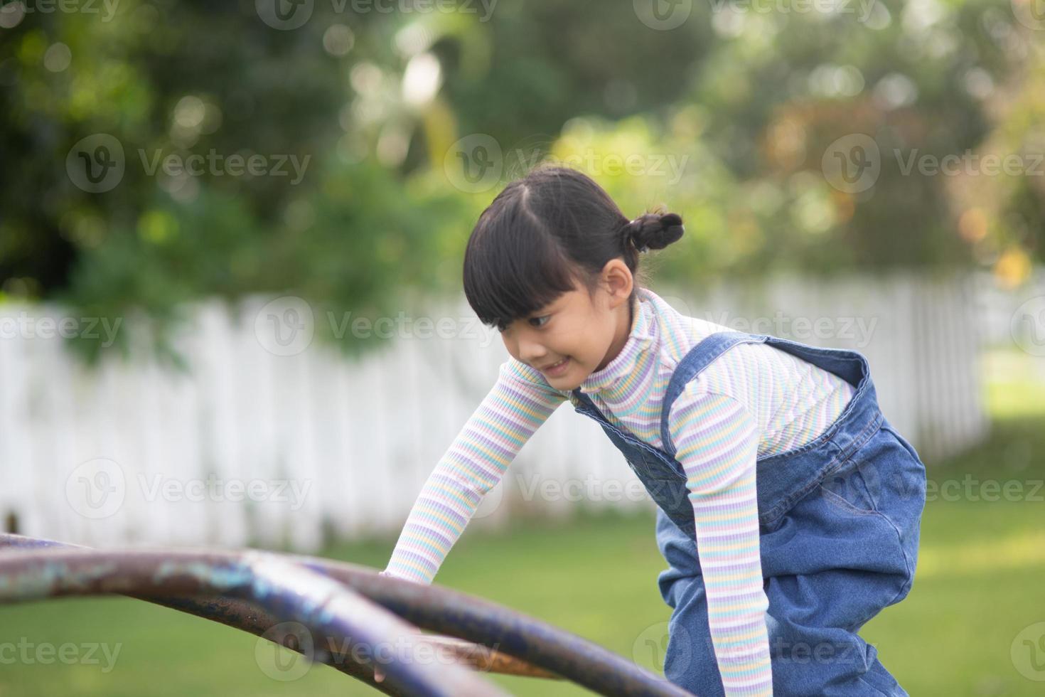 asiatico bambino ragazza giocando su il all'aperto terreno di gioco. bambini giocare nel scuola o scuola materna cortile. salutare estate attività per bambini. foto