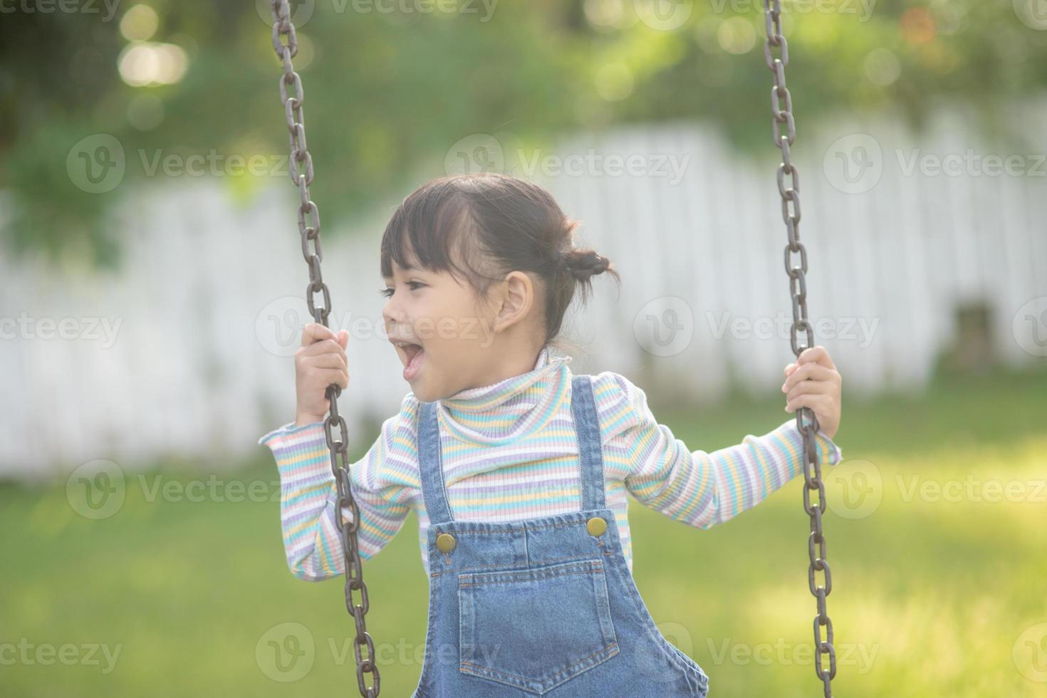 contento poco asiatico ragazza giocando swing all'aperto nel il parco foto