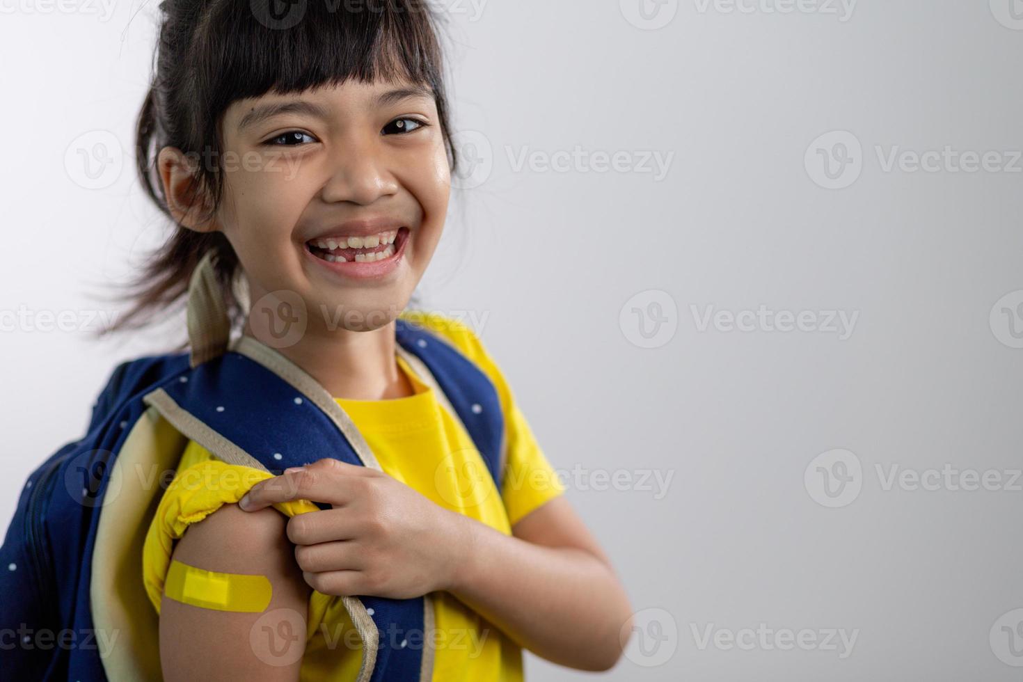 asiatico giovane ragazza mostrando sua braccio con giallo bendare dopo avuto vaccinati o inoculazione, bambino immunizzazione, covid delta vaccino concetto foto