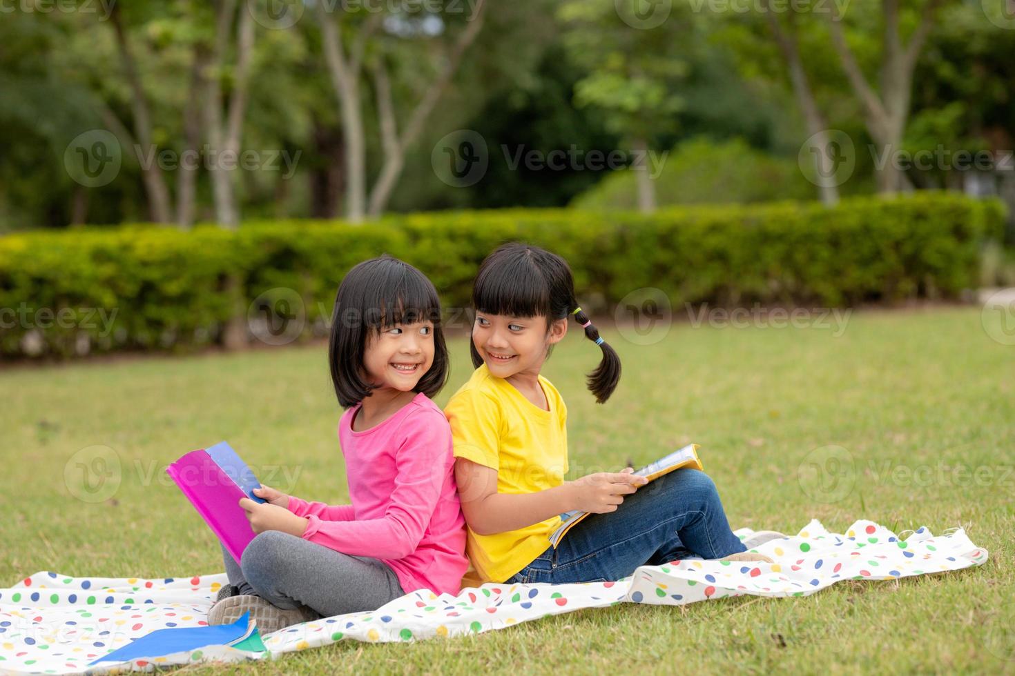 Due bellissimo poco ragazze lettura libri nel il giardino , seduta su erba. il concetto di formazione scolastica e amicizia. foto