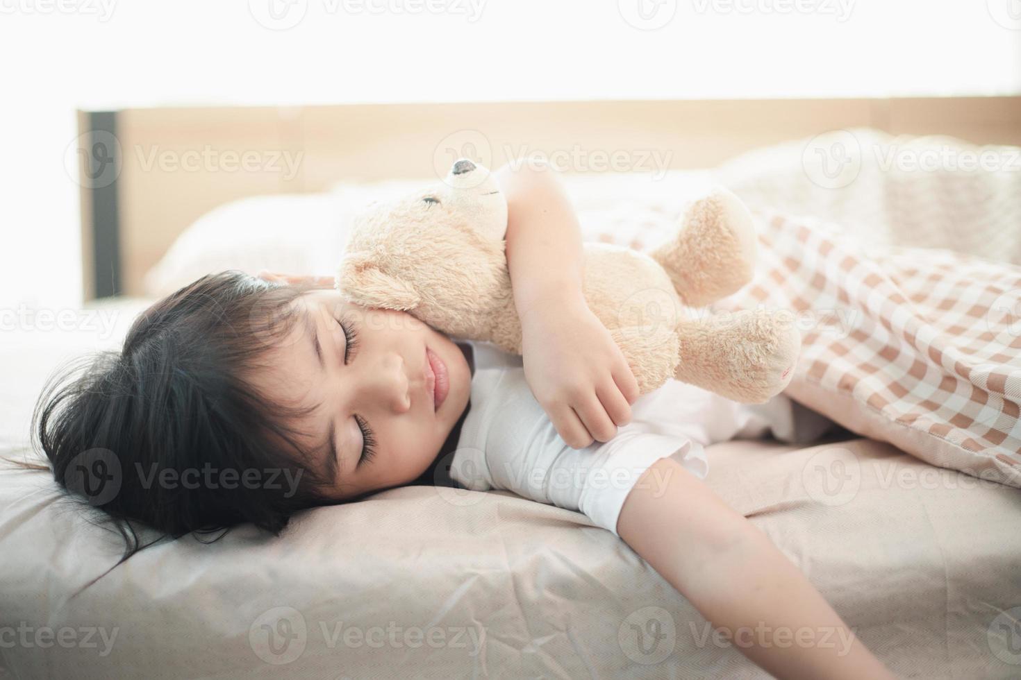 bambino poco ragazza dorme nel il letto con un' giocattolo orsacchiotto orso foto