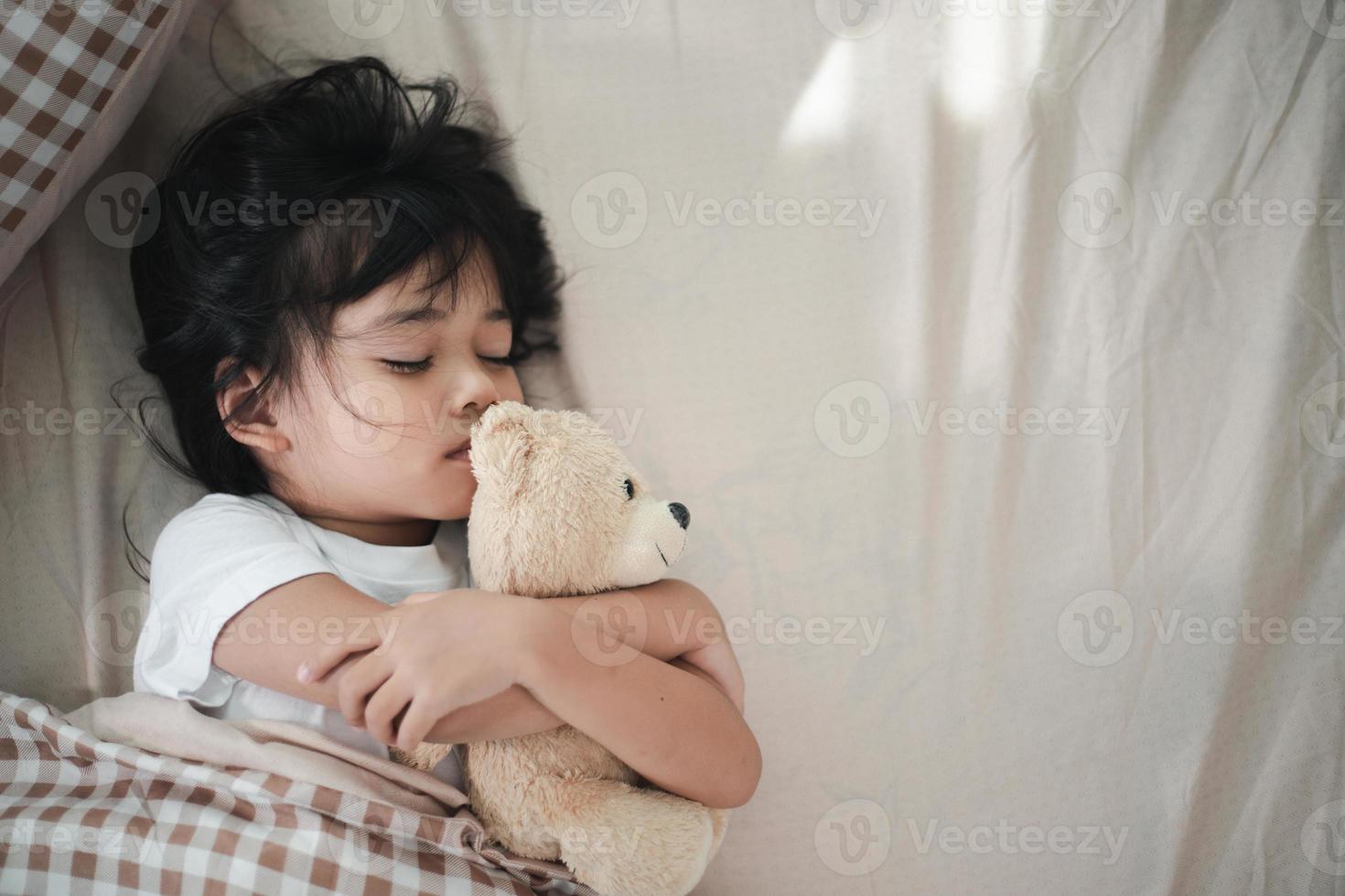 bambino poco ragazza dorme nel il letto con un' giocattolo orsacchiotto orso foto