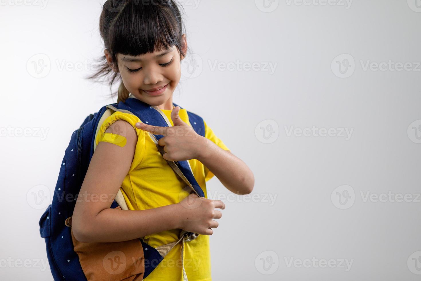 asiatico giovane ragazza mostrando sua braccio con giallo bendare dopo avuto vaccinati o inoculazione, bambino immunizzazione, covid delta vaccino concetto foto