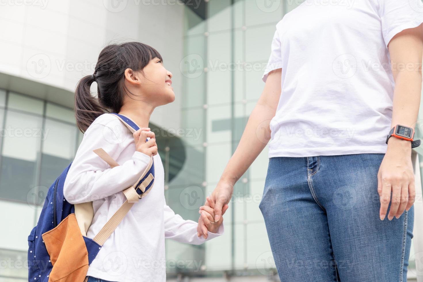 indietro per scuola. asiatico madre e figlia allievo ragazza con zaino Tenere mano e andando per scuola insieme. inizio di Lezioni. primo giorno foto