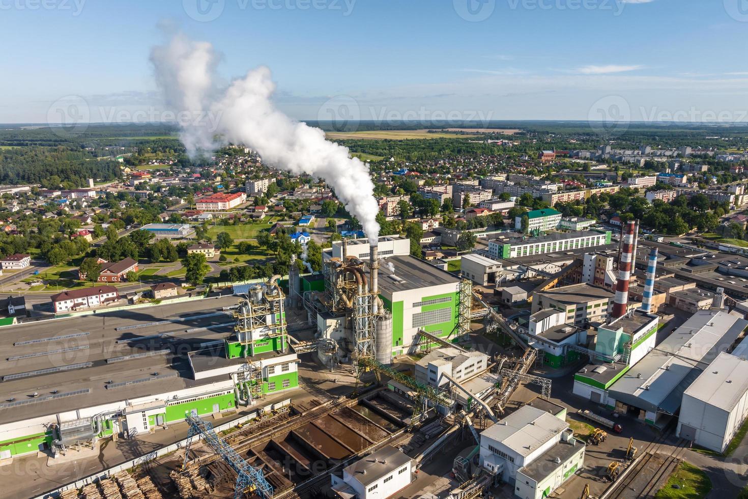 aereo panoramico Visualizza su Fumo tubi di un' la lavorazione del legno fabbrica su il banca di un' largo fiume foto