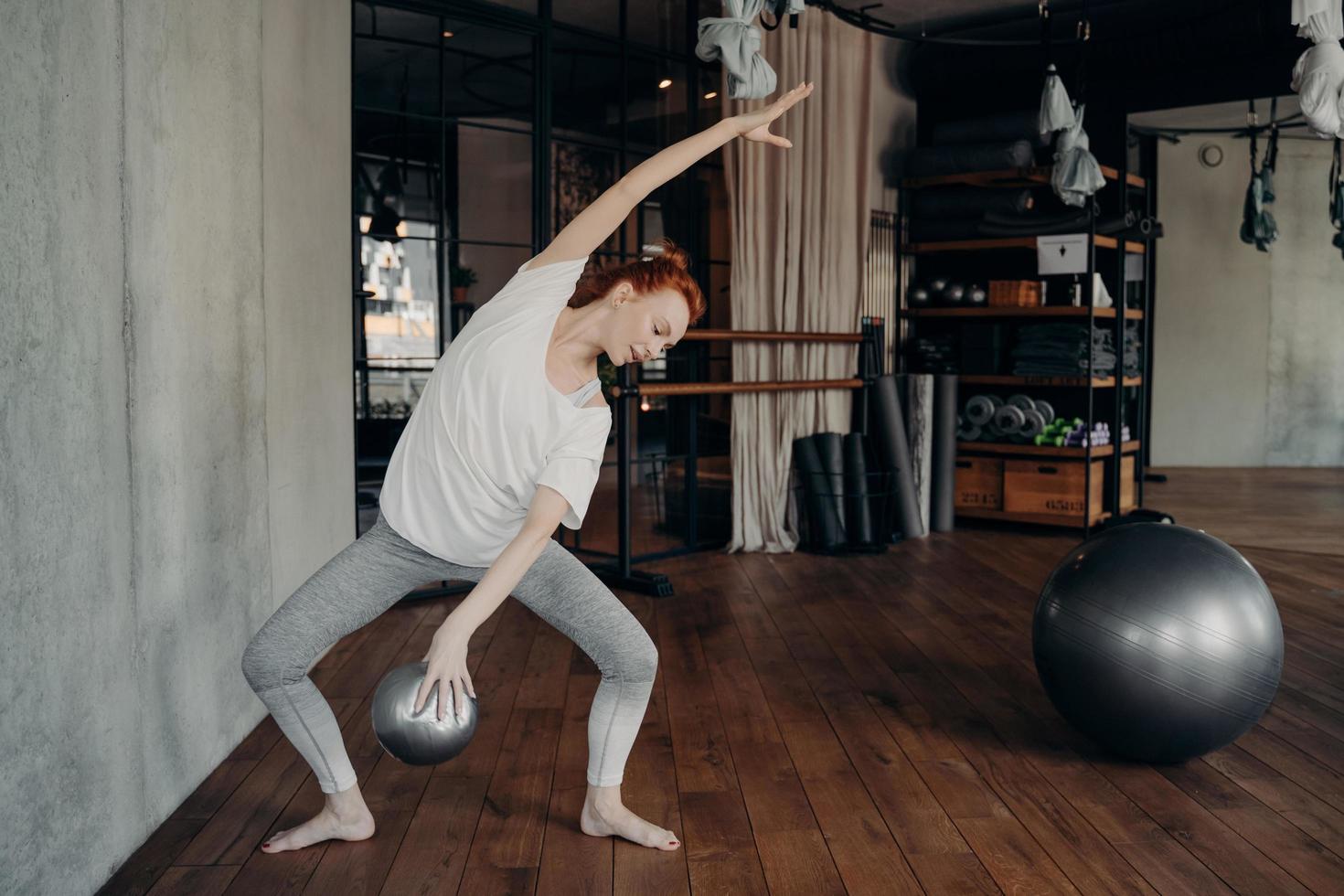 snella giovane ballerina dai capelli rossi che fa plié con un piccolo fitball in mano foto