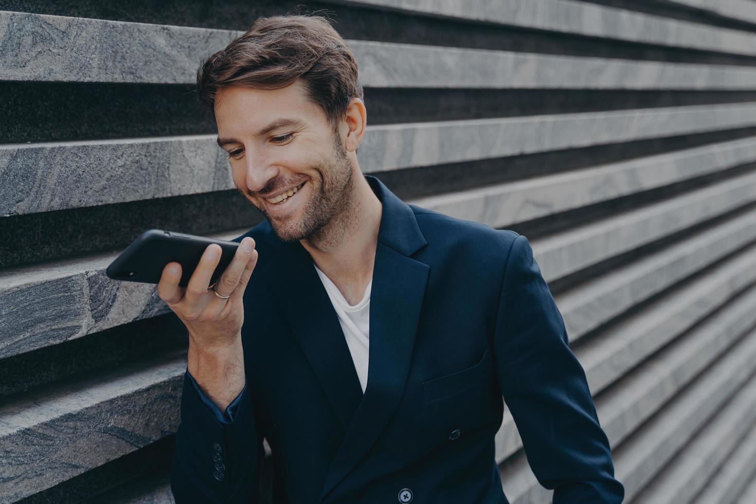 il giovane uomo attraente sta fuori e utilizza l'assistente di riconoscimento vocale sullo smartphone foto