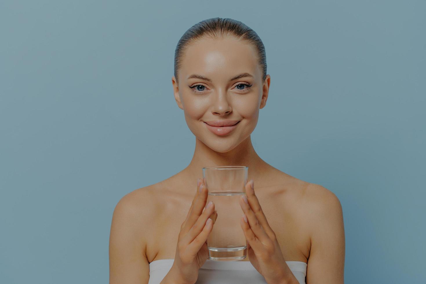 giovane donna affascinante con pelle e capelli dall'aspetto sano con in mano un bicchiere di acqua minerale pulita foto