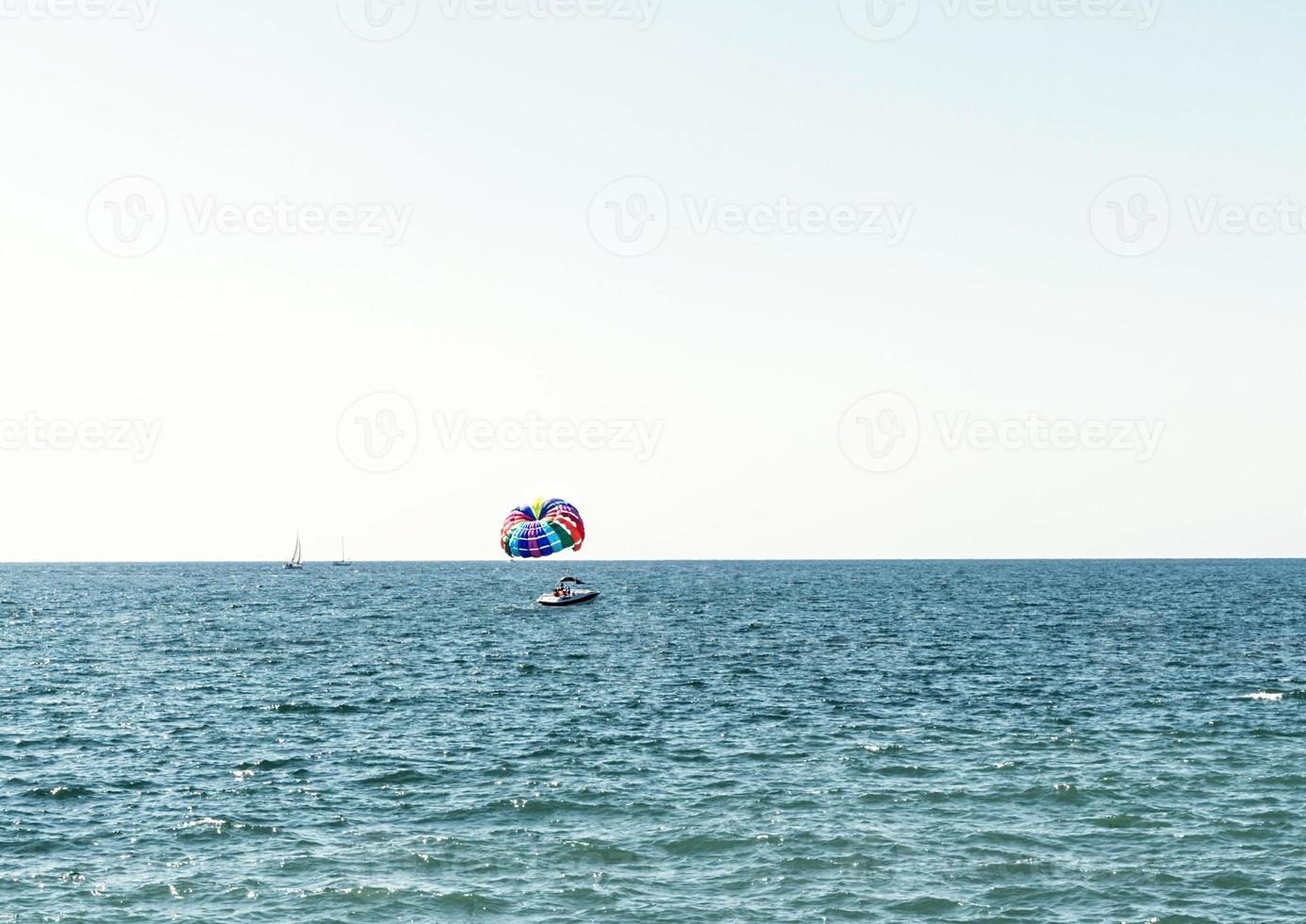 parasailing multicolore arcobaleno paracadute dietro a barca al di sopra di blu turchese mare paesaggio estate attività copia spazio selettivo messa a fuoco foto