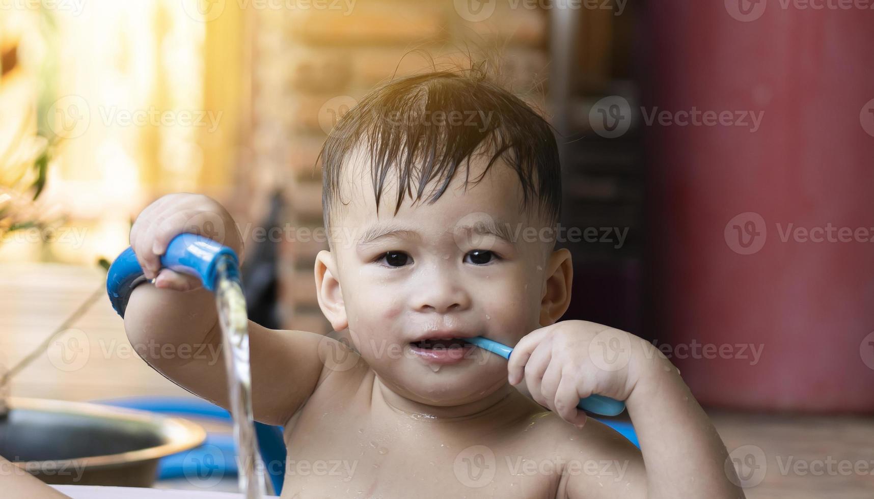 carino poco ragazzo assunzione un' doccia e spazzolatura il suo denti nel il mattina. contento bambini giocando e bagnarsi al di fuori il Casa concetto. asiatico ragazzi viso è sorridente e contento. prendere un' doccia utilizzando un' tubo flessibile foto