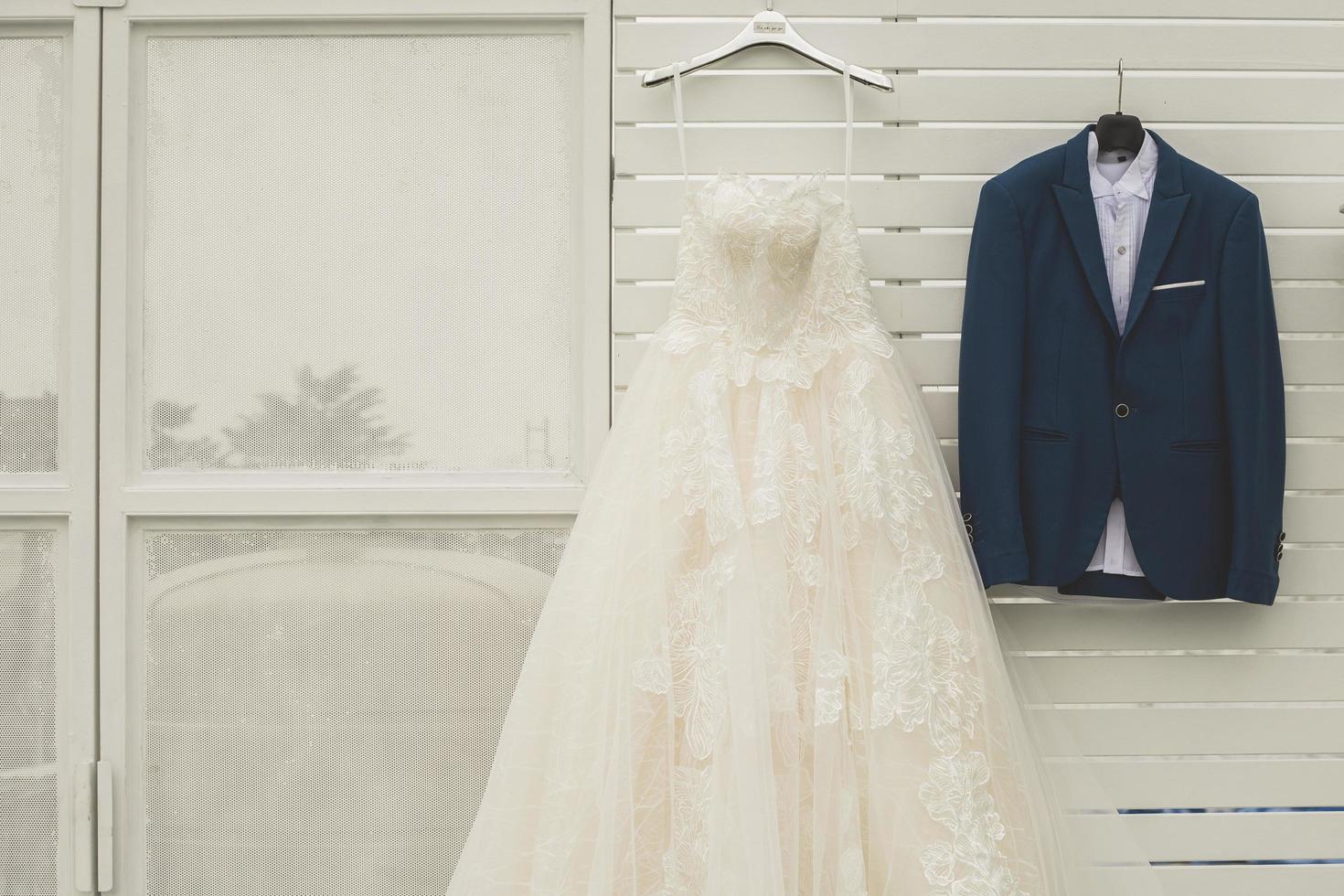 sposo completo da uomo e bridal vestito sospeso su bianca stecca parete nel nozze cerimonia giorno, lusso costume su bianca sfondo foto