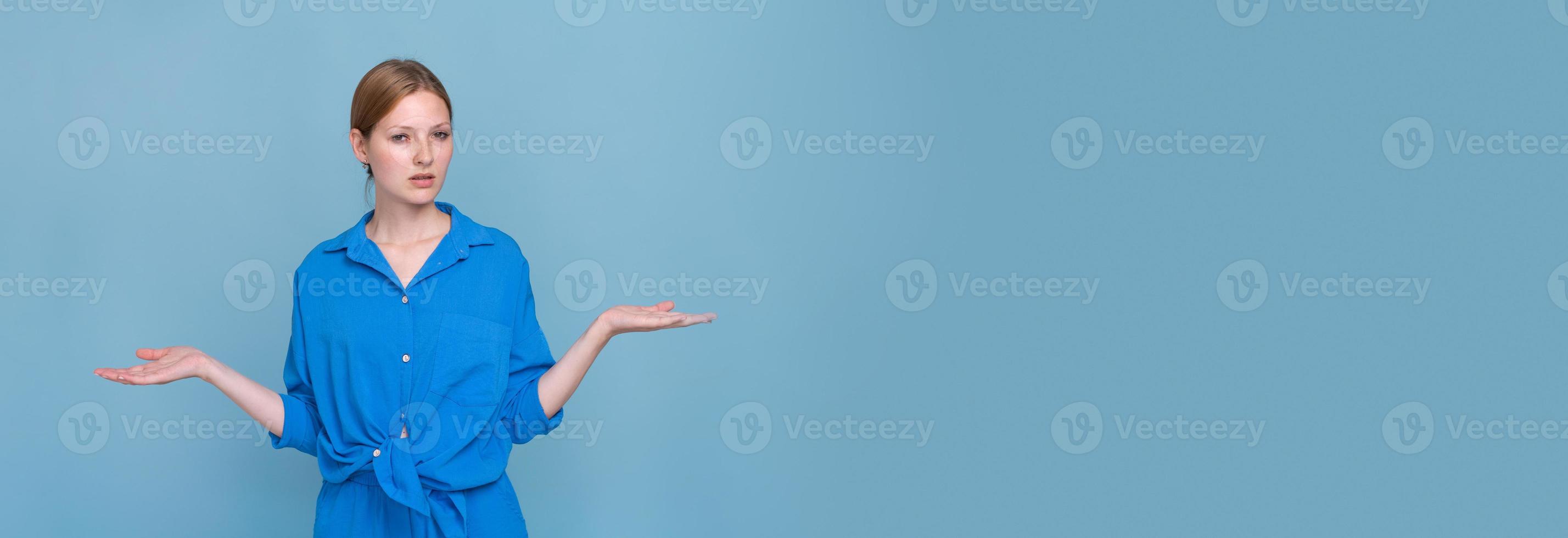 giovane donna nel camicia su blu sfondo, puntamento per lato con tutti e due mani foto