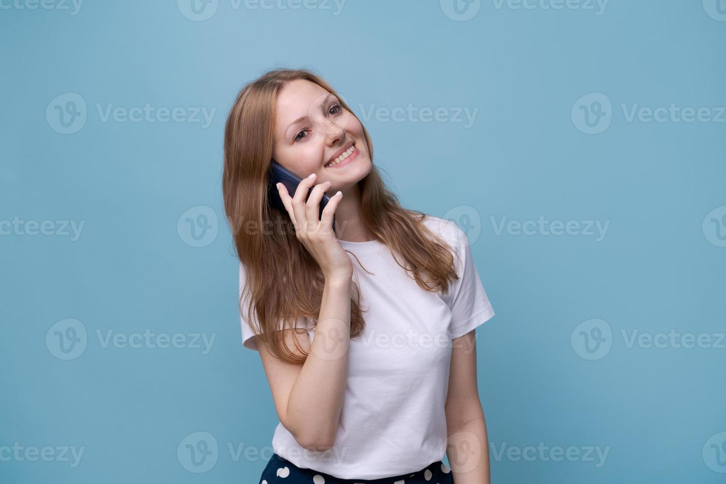 gioioso caucasico giovane donna parlando su Telefono su un' blu sfondo, mobile foto