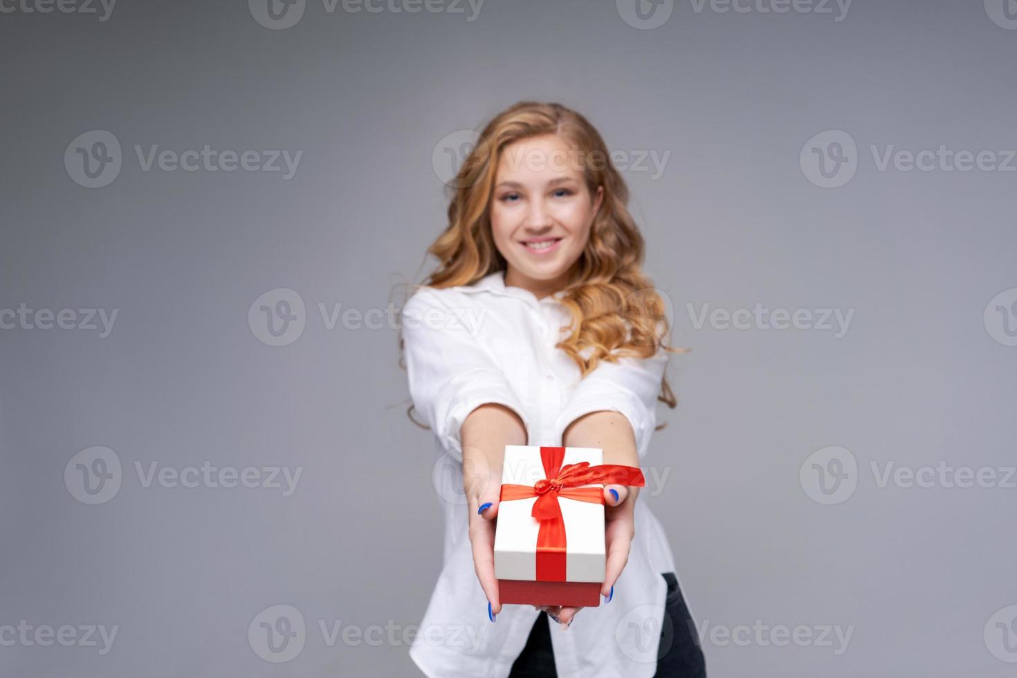 ritratto un attraente contento divertente ragazza Tenere regalo scatola su leggero grigio foto