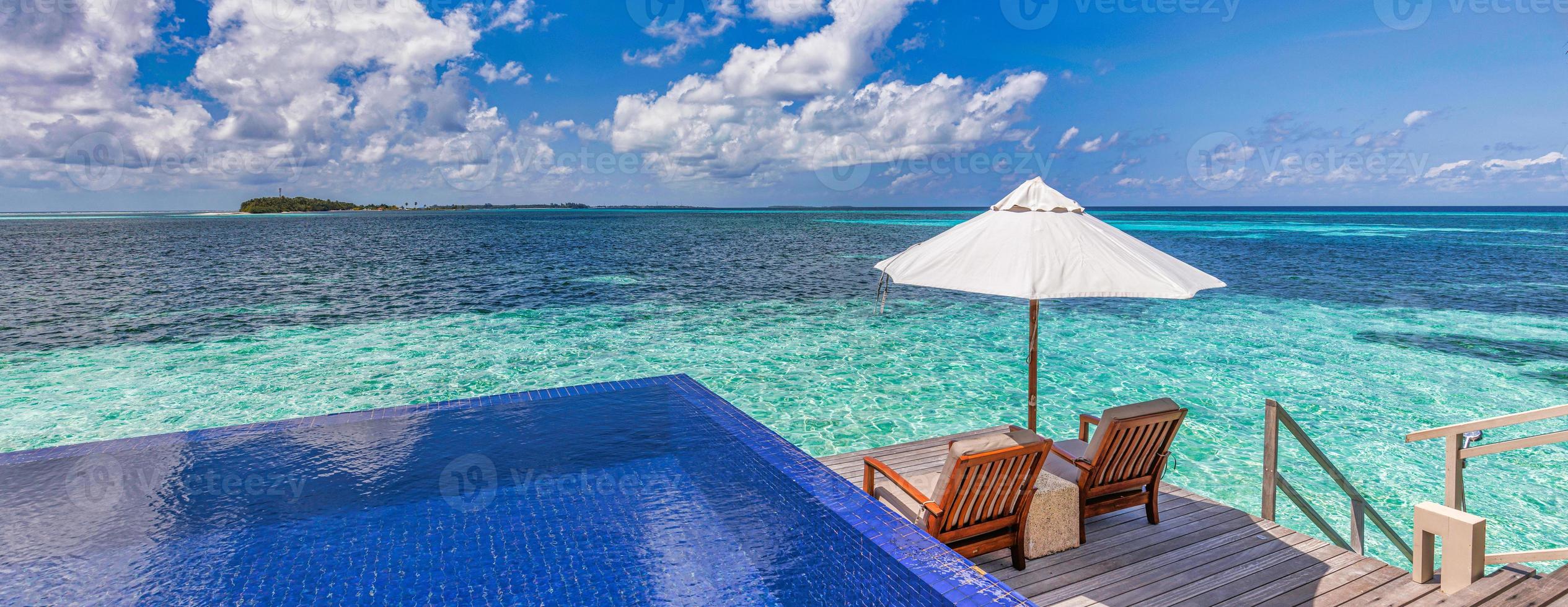 Maldive lusso spiaggia ricorrere. infinito nuoto piscina, spiaggia sedie o lettini sotto ombrelli nel al di sopra di acqua villa. blu cielo, sorprendente laguna. estate vacanza, viaggio vacanza. panoramico bandiera foto