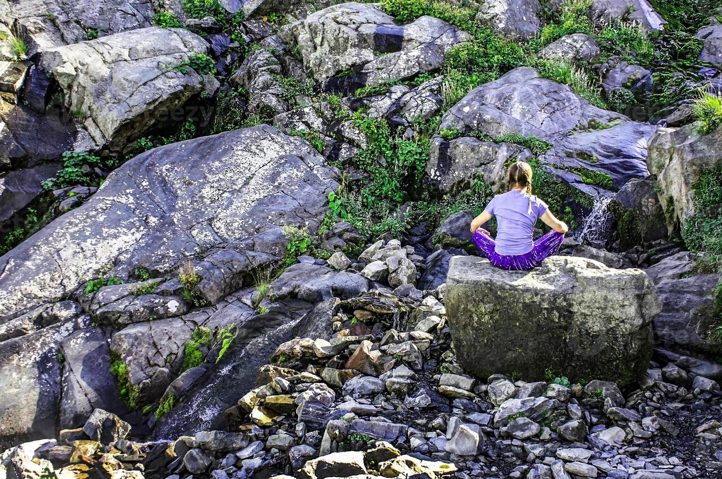 giovane biondo donna a partire dal il indietro seduta su un' pietra e Meditare nel il montagne. donna a partire dal dietro. silenzio di mente foto