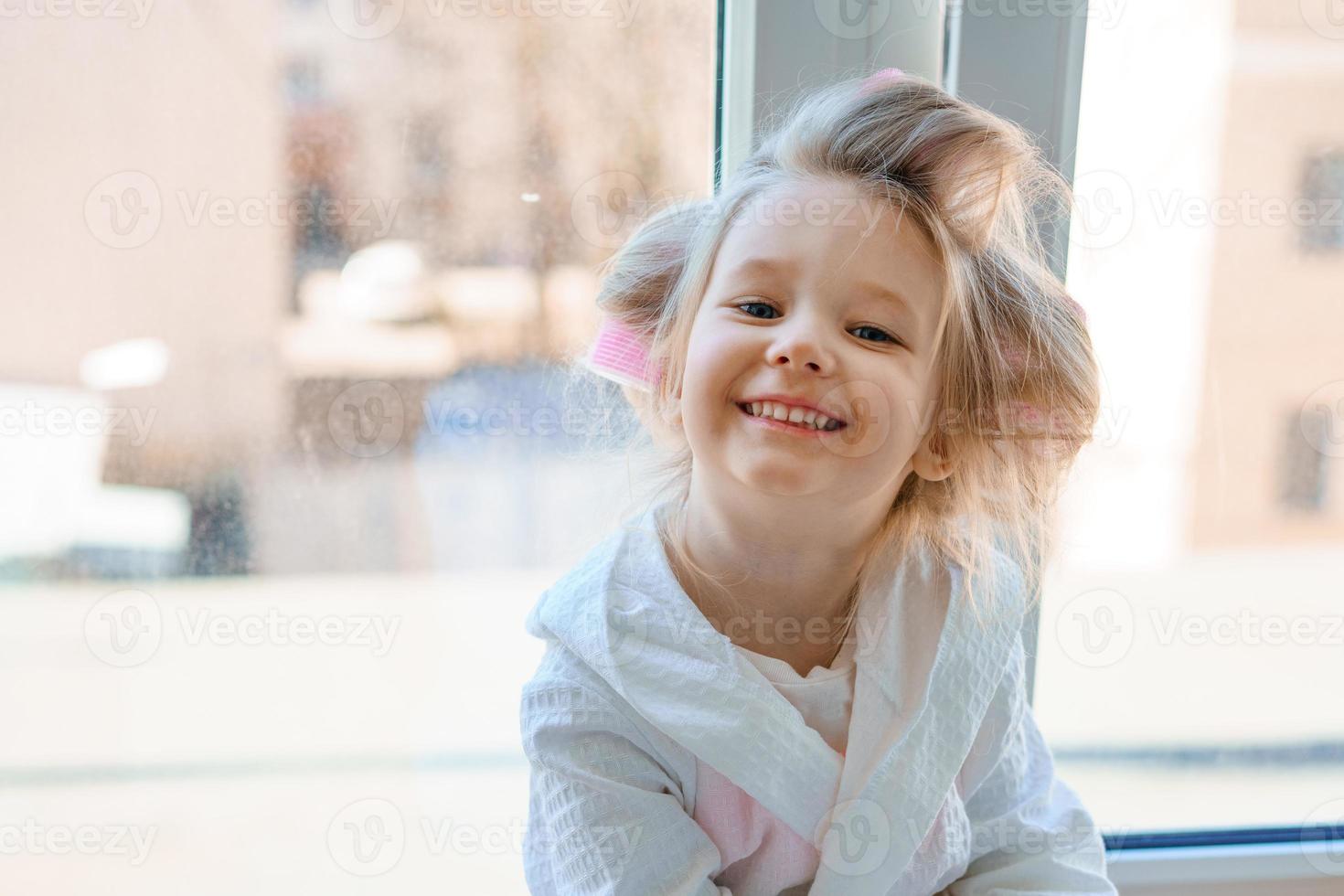 allegro poco ragazza nel capelli bigodini su il sfondo di il finestra foto