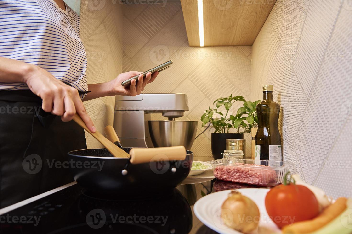 donna cucinando salsa bolognese e uso smartphone foto