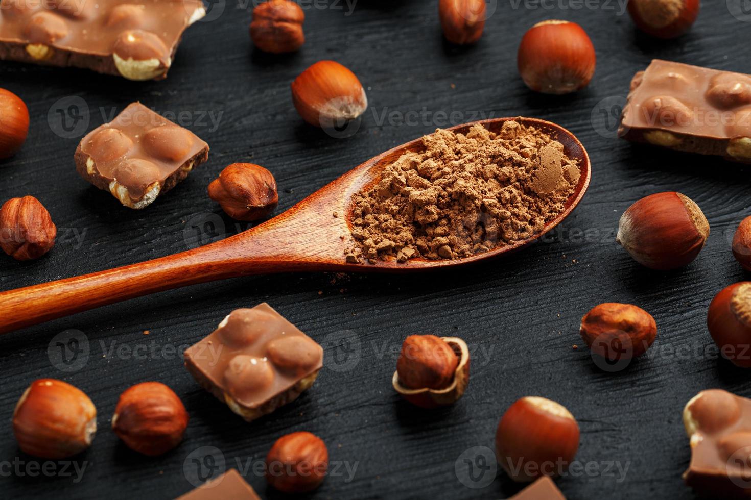 cioccolato con Nocciole e un' di legno cucchiaio con cacao su un' buio sfondo, circondato di noccioline nel il conchiglia e pelato. foto