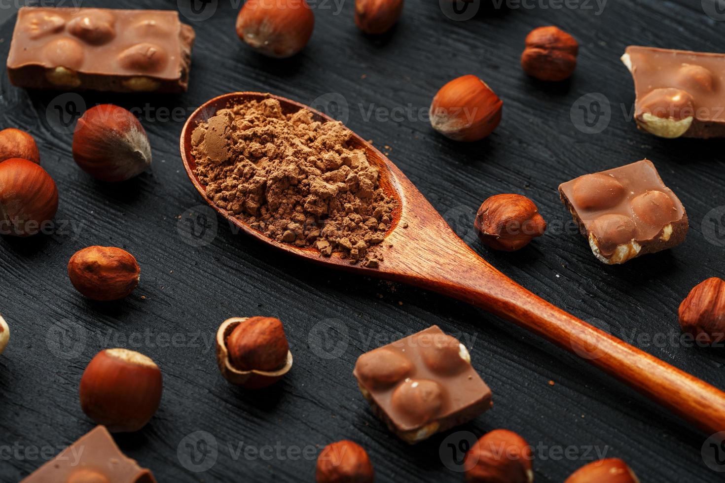 cioccolato con Nocciole e un' di legno cucchiaio con cacao su un' buio sfondo, circondato di noccioline nel il conchiglia e pelato. foto