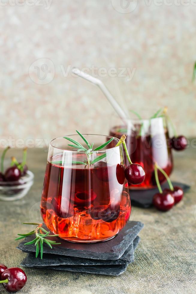 cocktail con ciliegia, rosmarino e ghiaccio nel bicchieri su il tavolo. fatti in casa mocktail. verticale Visualizza foto