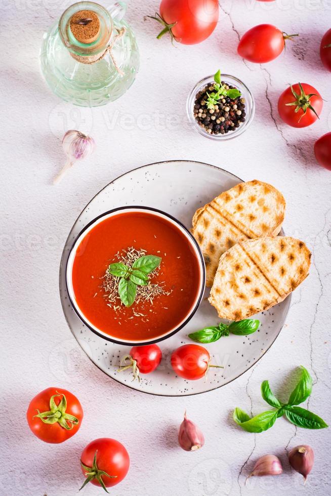 ciotola con fatti in casa pomodoro la minestra con basilico e fresco verdure su il tavolo. superiore e verticale Visualizza foto