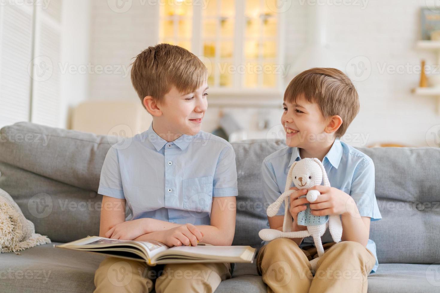 un più vecchio fratello è lettura libro per il suo minore fratello seduta su divano. foto