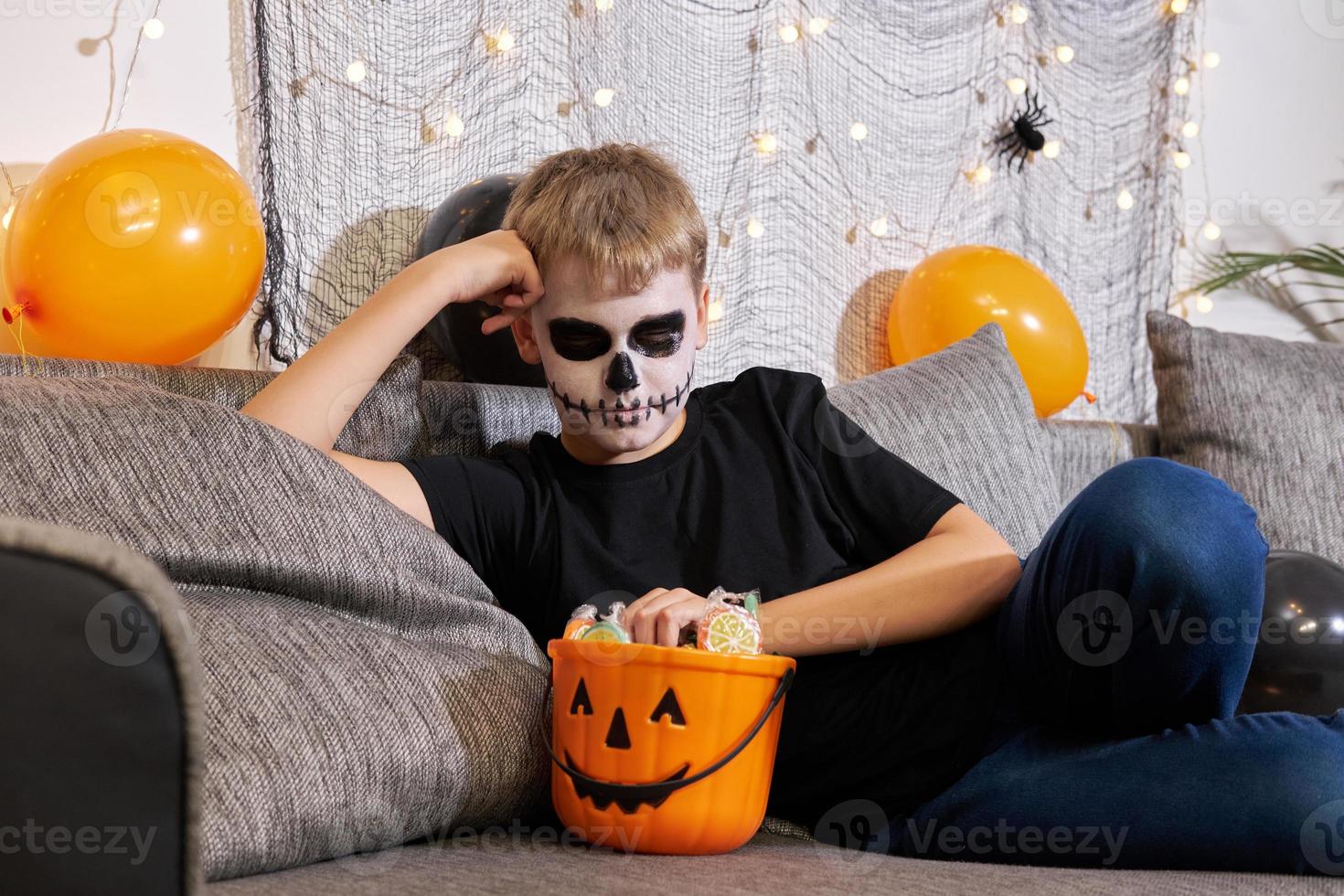 un' ragazzo nel scheletro trucco tira su caramella a partire dal un' Halloween festa. foto