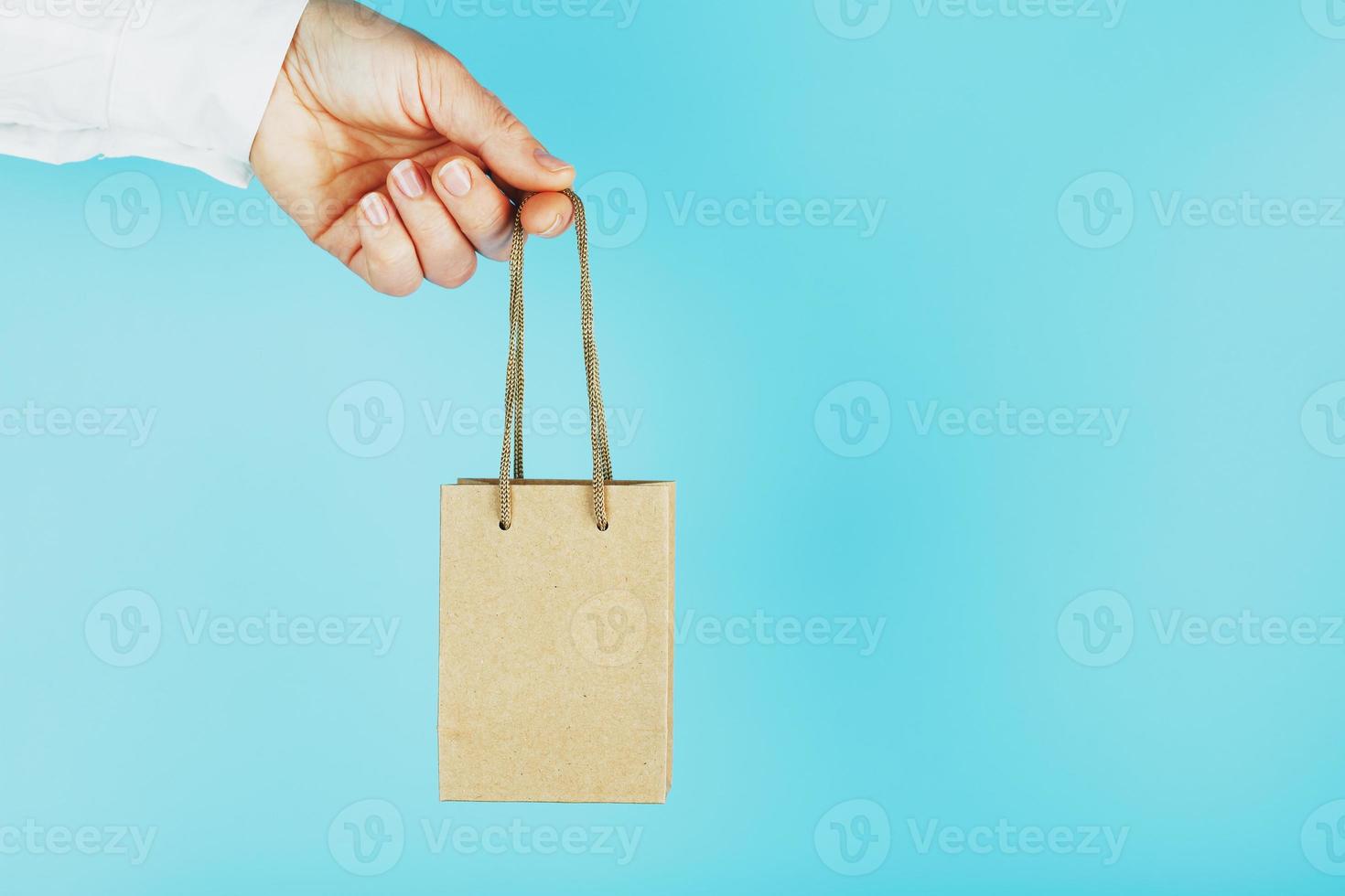 un' piccolo carta Borsa a braccia lunghezza, su un' blu sfondo. disposizione di il confezione modello con spazio per copiando, pubblicità. foto