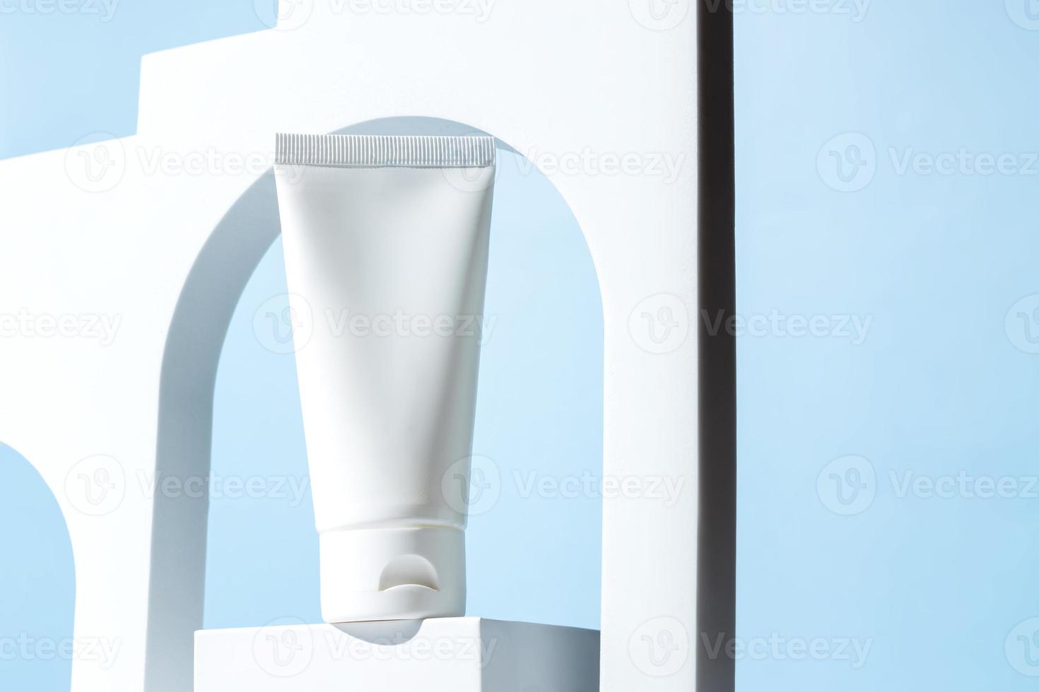 bianca senza marchio plastica spremere tubo per crema o shampoo sta su bianca podio nel bianca arco su blu sfondo. cosmetici vetrina. modello foto