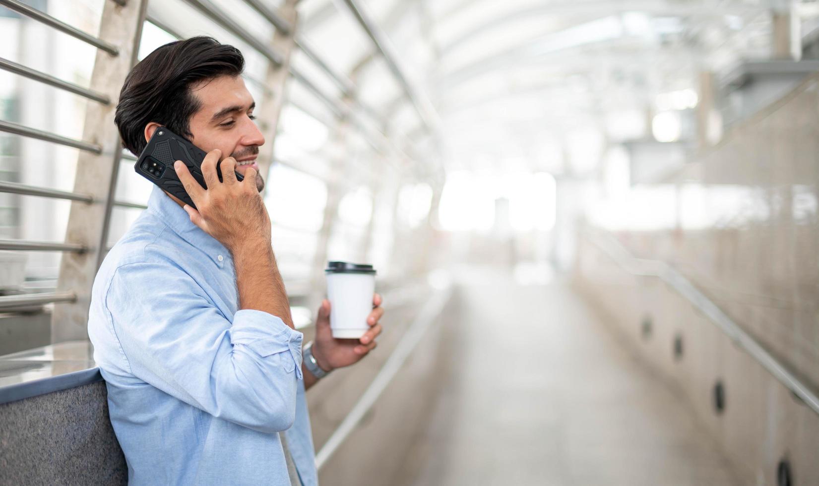 il uomo Tenere un' tazza di caffè e utilizzando un' smartphone e parlando con il suo amico mentre lui in attesa il suo amico a il aeroporto. foto