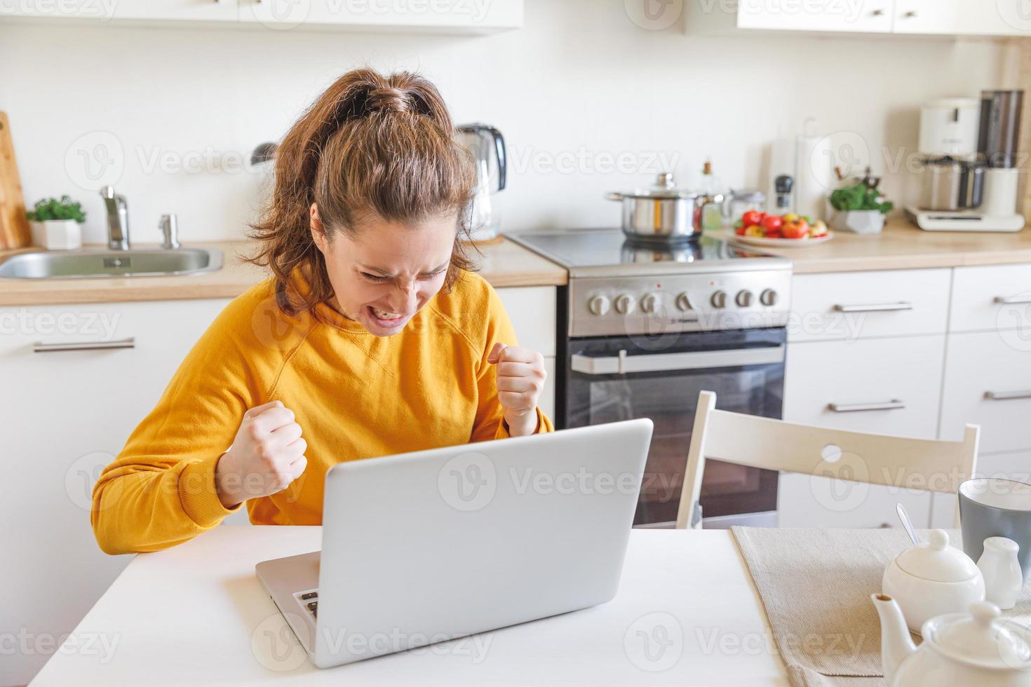 mobile ufficio a casa. arrabbiato infastidito donna Lavorando utilizzando su il computer portatile e urlando seduta nel cucina a casa. giovane stressato ragazza studiando o Lavorando al chiuso. libero professionista attività commerciale quarantena concetto. foto