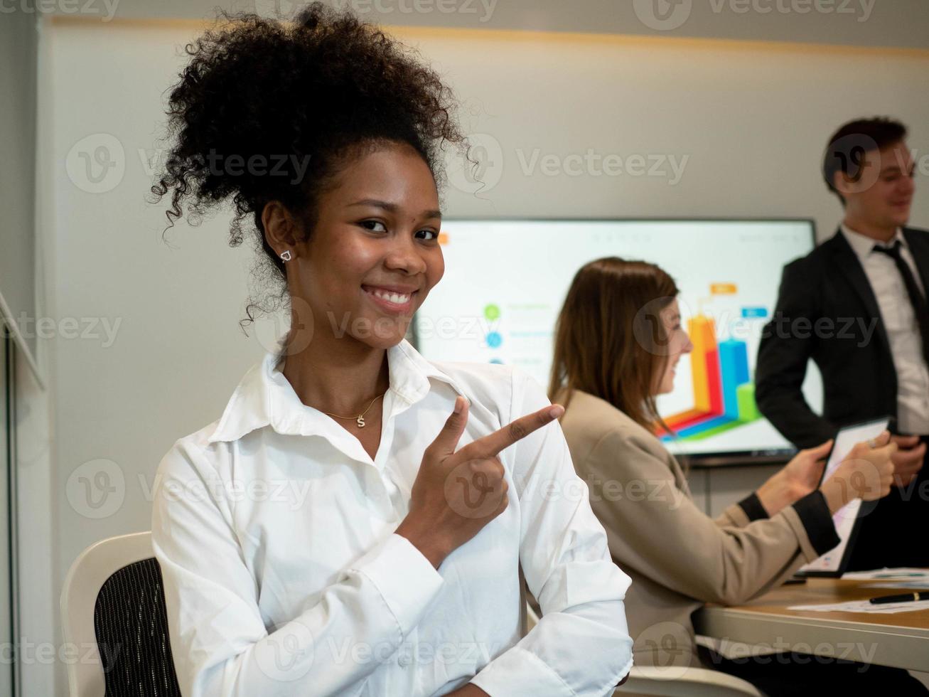 donna d'affari femmina donna nero africano americano persona afro capelli seduta interno camera azienda ufficio contento Sorridi puntamento dito allegro incontro conferenza camera opera lavoro carriera foto