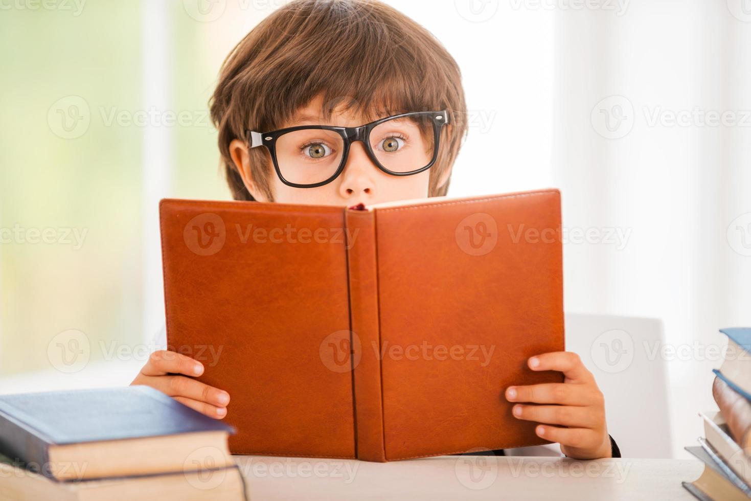sorprendente storia sorpreso poco ragazzo lettura un' libro mentre seduta a il tavolo foto