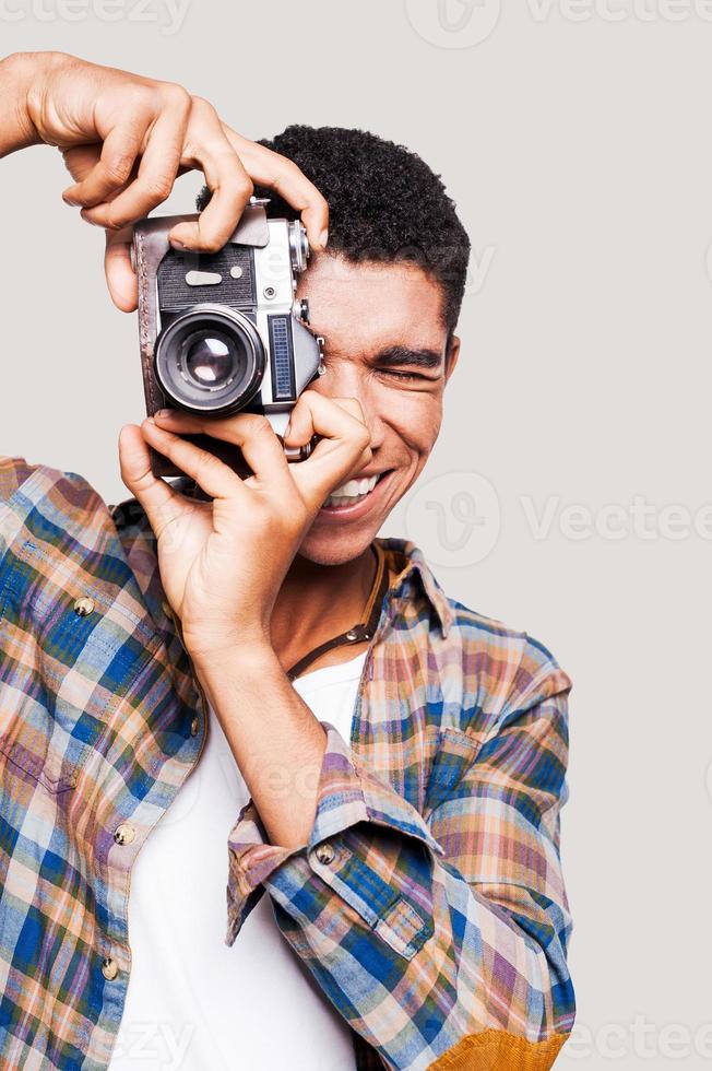 dare me un' Sorridi bello giovane afro americano uomo assunzione un' immagine e sorridente mentre in piedi contro grigio sfondo foto
