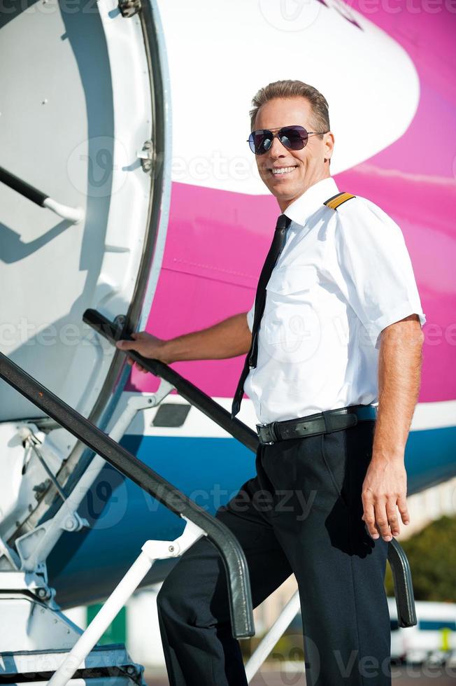 pronto per volo fiducioso maschio pilota nel uniforme andando in il aereo e sorridente foto