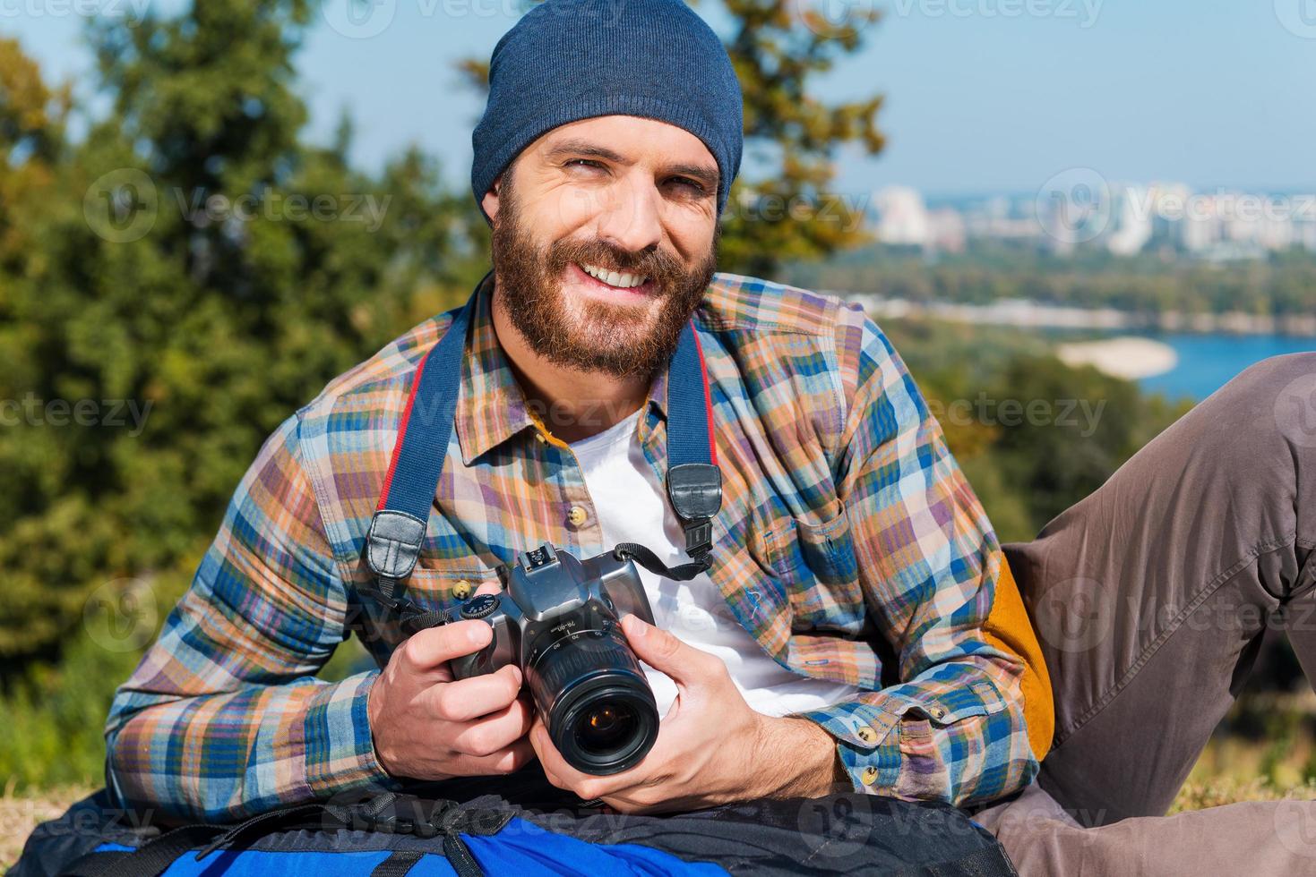 in viaggio è impossibile senza telecamera. bello giovane uomo dire bugie su il zaino e Tenere telecamera foto