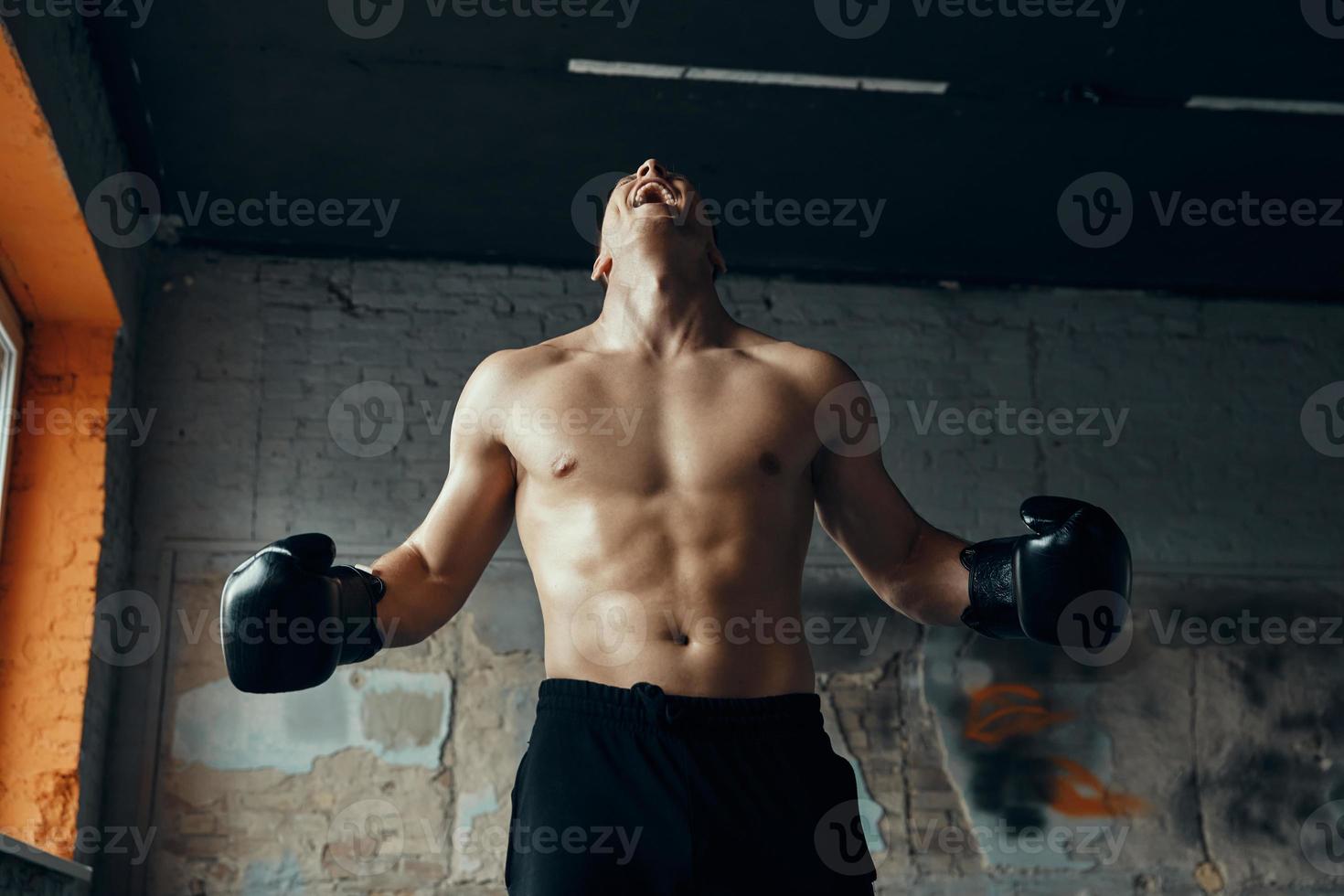 furioso giovane uomo nel boxe guanti urlando mentre in piedi nel Palestra foto