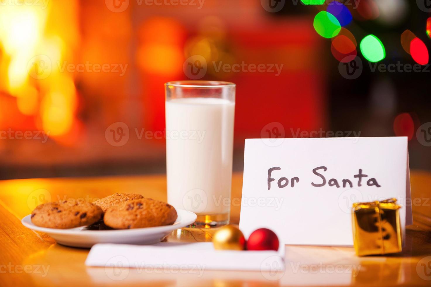 per babbo natale. avvicinamento di biscotti e bicchiere di latte su il tavolo con Natale albero e camino nel il sfondo foto