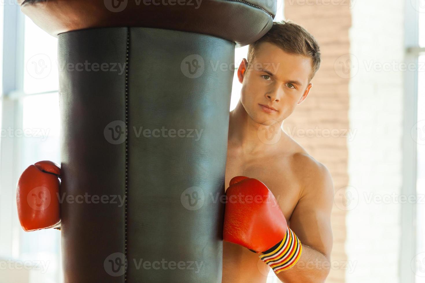 energia dentro me. fiducioso giovane pugile nel gli sport guanti pendente a il punzonatura Borsa e guardare a telecamera foto