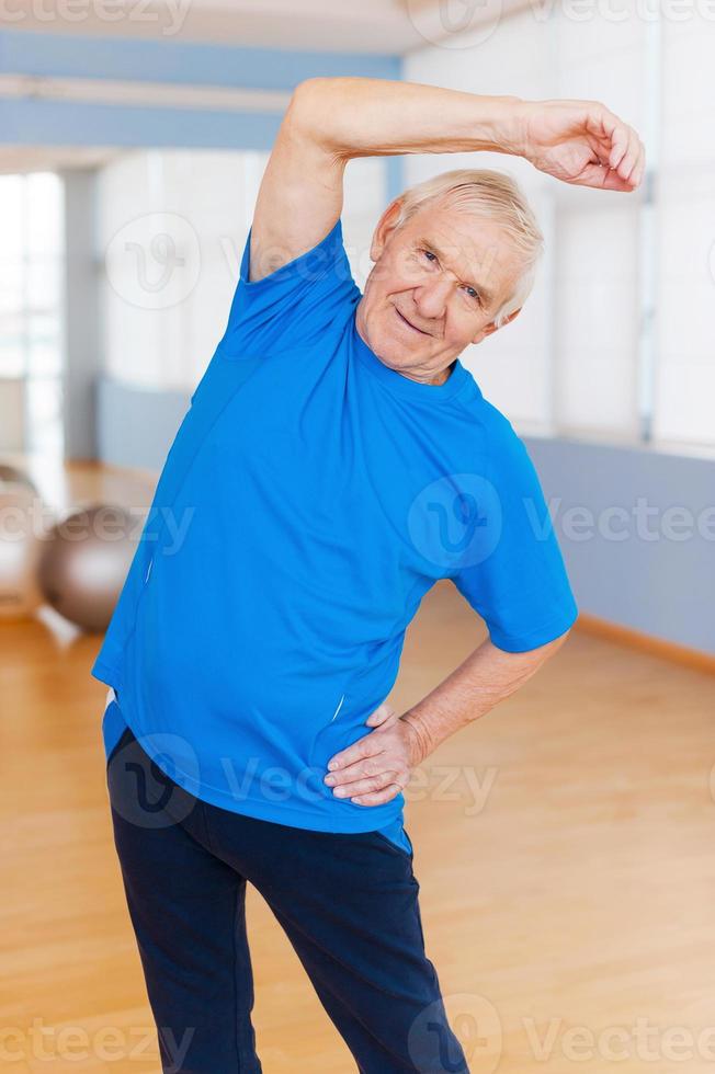 soggiorno attivo. allegro anziano uomo fare allungamento esercizi e sorridente mentre in piedi in casa foto