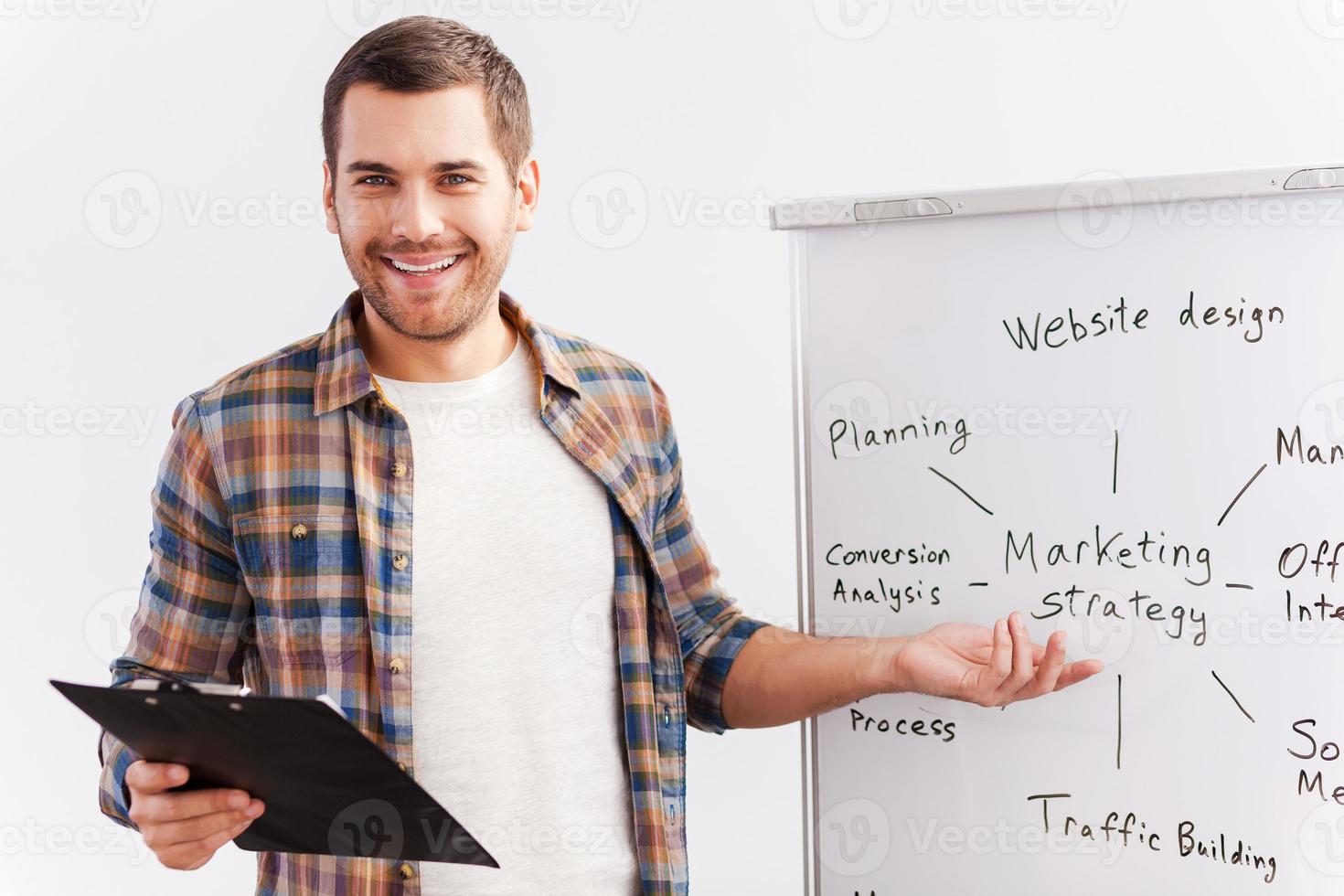 parlando di strategia. fiducioso giovane uomo nel inteligente casuale indossare in piedi vicino lavagna e puntamento esso con Sorridi foto