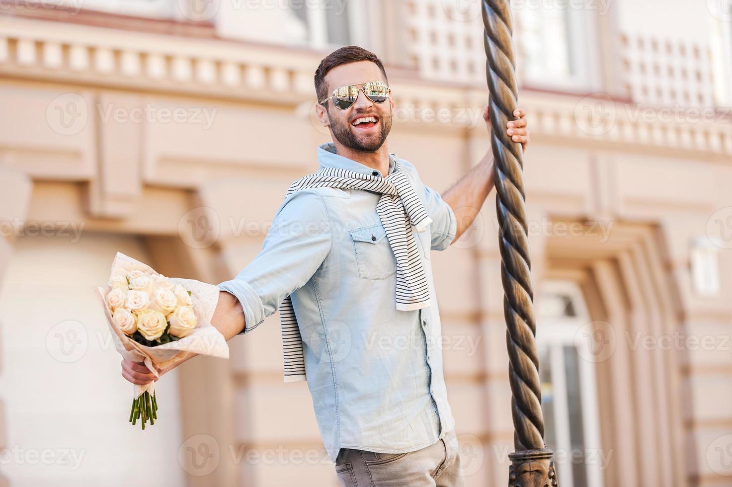 io am nel amore contento giovane uomo Tenere mazzo di fiori e guardare a telecamera mentre pendente a il colonna all'aperto foto