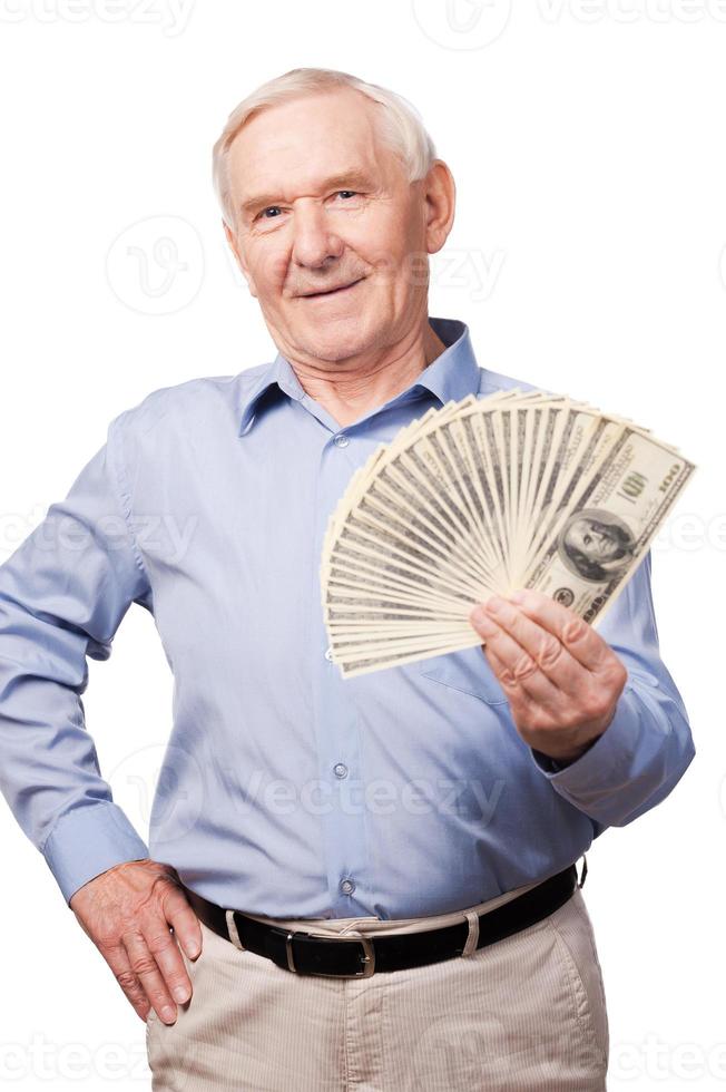 mondo di ricco uomini. ritratto di anziano uomo sorridente a telecamera e Tenere i soldi nel il suo mani mentre in piedi contro bianca sfondo foto