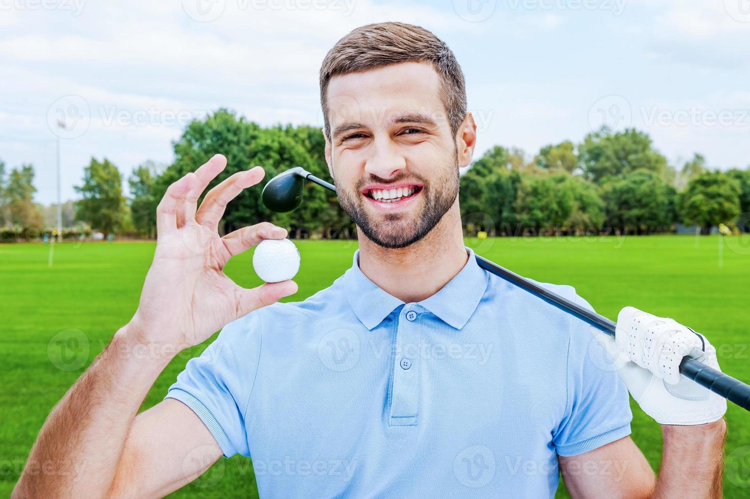riuscito giocatore di golf. contento giovane uomo Tenere golf palla e autista mentre in piedi su verde foto